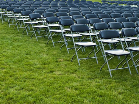 Fold up metal chairs arraged in rows for an event in a park.