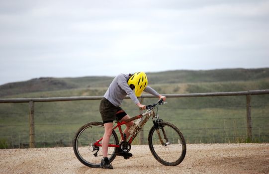 Mud-splattered mountain biker against a dirt road and green pasture.