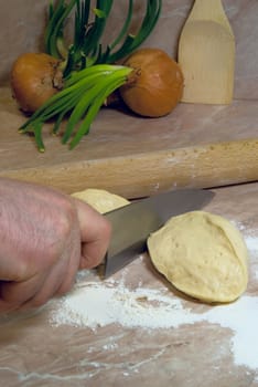 Slicing yeast dough on two pieces with onions on background