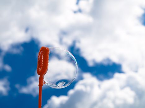 Bubble wand with one soap bubble against blue sky with clouds