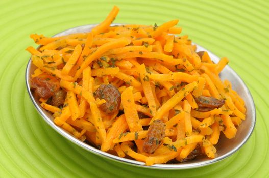 Grated carrots with raisins in a bowl on a green place mat