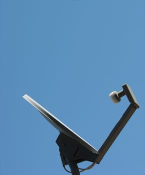 A satellite dish against a clear blue sky, horizontal orientation, listening.