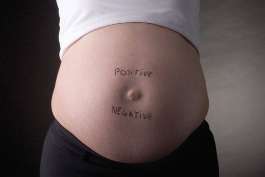 seven month pregnant belly with positive and negative written on stomach