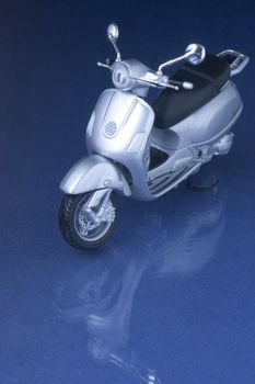 Toy vespa scooter hovering over a blue reflecting surface