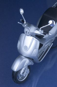 Toy vespa scooter hovering over a blue reflecting surface