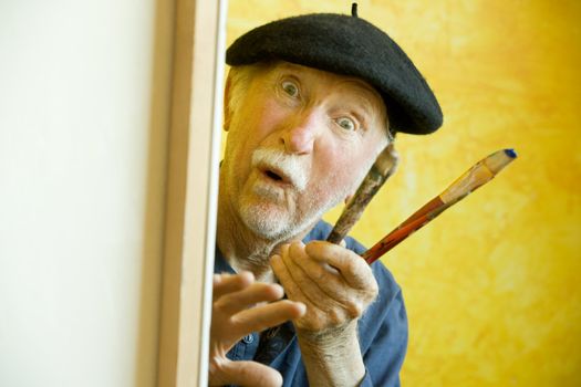 Elderly painter wearing a beret working on a large canvas and looking up