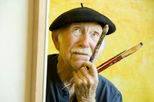 Elderly painter wearing a beret working on a large canvas and looking up