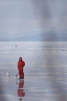 Lonely fisherman dress in red on frost lake