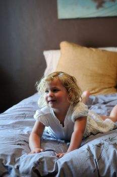 A happy little girl with blonde hair and a white dress plays on her parents bed