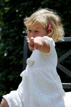 Little girl points at the viewer while sitting in a garden chair.