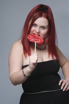 Red hair female model in goth look bitting on big red lollipop