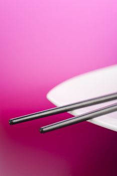 Chopsticks on the white plate over pink background