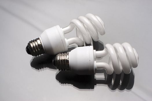 two compact fluorescent light bulb on reflective surface