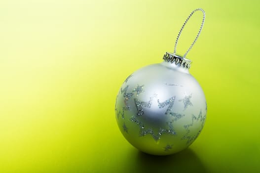 Silver Christmas bulb sitting on a green background.