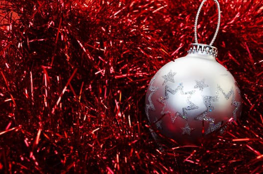 Silver Christmas bulb sitting on a red metal background.