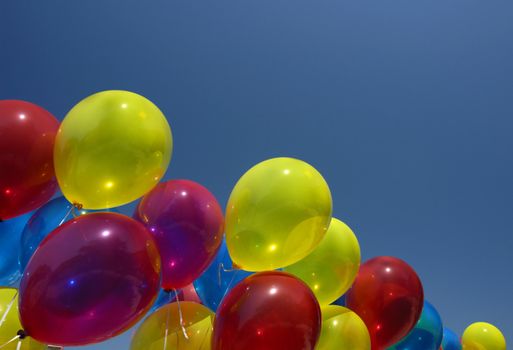 A row of multi-coloured balloons strianing against their tethers. Space for text in the sky.
