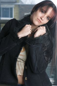 Twenty something fashion model in rock style looking down, standing in from of a widow with urban background 