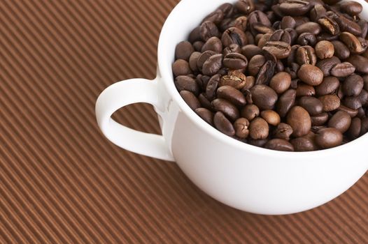 White coffee cup full of coffee beans over a curly brown background