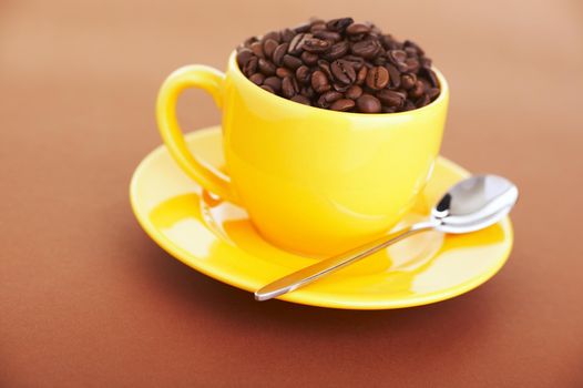 Yellow coffee cup filled with beans over a brown background