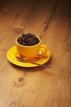 Yellow coffee cup filled with beans on a wooden table