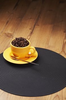 Yellow coffee cup filled with beans on a wooden table