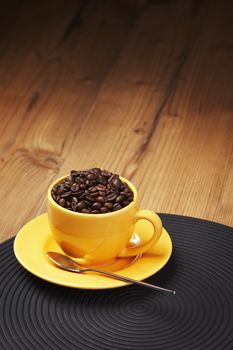 Yellow coffee cup filled with beans on a wooden table