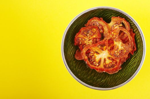 Dried sliced tomatoes in green bowl on the yellow background.