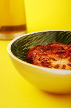 Dried sliced tomatoes in green bowl on the yellow background.