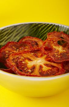 Dried sliced tomatoes in green bowl on the yellow background.
