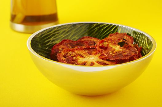 Dried sliced tomatoes in green bowl on the yellow background.