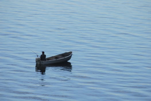 A fisherman sits alone in his boat in the early morning. Space for text.