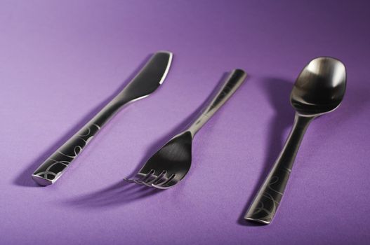 Modern spoon, fork and knife on purple table. 