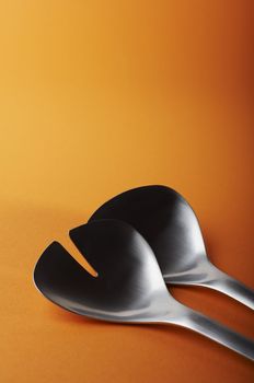 big salad spoon and fork on orange background