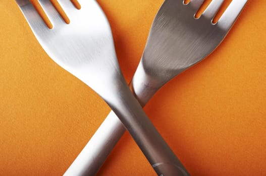 Two crossed forks over a orange background