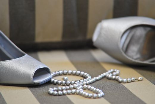 Formal silver shoes and string of pearls on a surface with lines