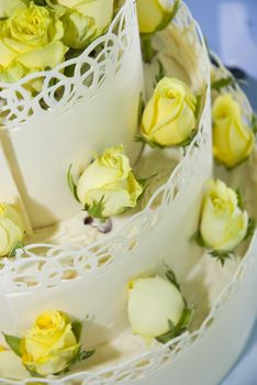 White three-tiered wedding cake decorated with light yellow roses