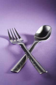 Crossed spoon and fork on purple table
