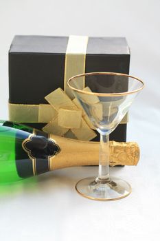A black boxed gift with a golden bow and a bottle of champagne