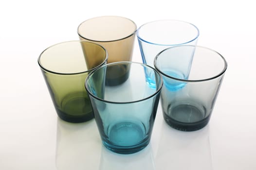 Colorful water glasses in circle formation over a white reflective background