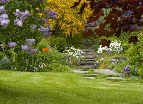 Idyllic garden with stone path and stairs, bushes, trees and flowers.