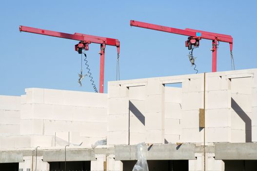 Two red mini cranes on a construction site for residential buildings.