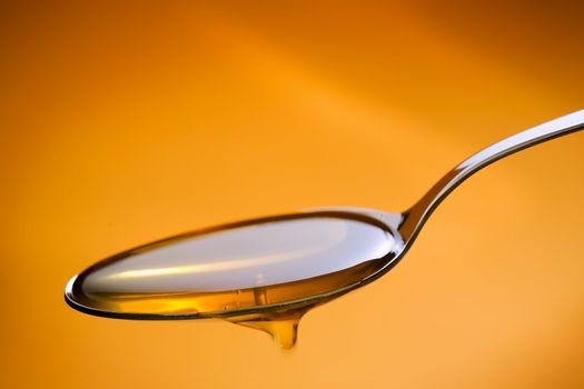 Metal spoon filled with honey over a orange background