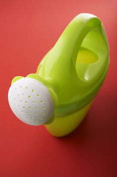 Green toy watering can on red background