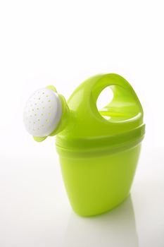 Green toy watering can on white glossy background with reflection