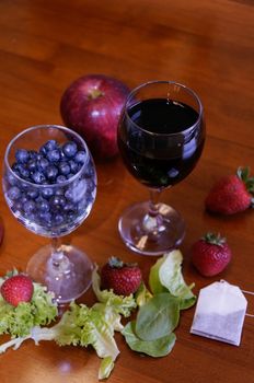 Blueberries and wine in wine glasses with other fruits surrounding them.