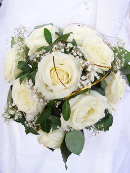 There is wedding bouquet of the white roses in the hands of bride.