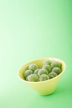 Green marmalade balls in the bowl on the green background