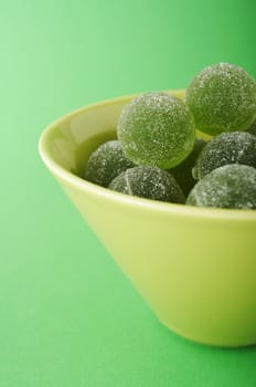 Green marmalade balls in the bowl on the green background
