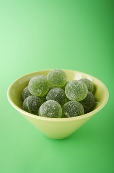 Green marmalade balls in the bowl on the green background