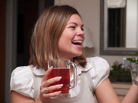 Young attractive woman drinking a hot cup of tea and laughing